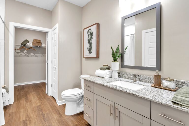 Modern bathroom with granite countertop, large mirror, plant decor, and wood flooring. Elegant and minimalist design.