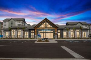 New commercial building with Now Open sign at sunset, surrounded by palm trees and blue sky.