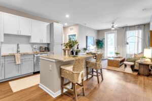 Modern open-concept kitchen and living room with island seating, white cabinets, and wood flooring. Bright and inviting space.