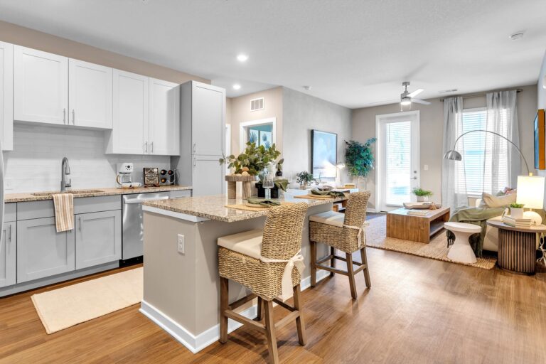 Modern open-concept kitchen and living room with island seating, white cabinets, and wood flooring. Bright and inviting space.