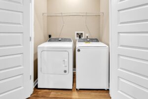 Laundry room with a modern washer and dryer on wooden floor, white doors open.