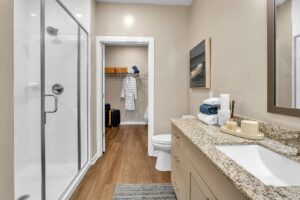 Modern bathroom with glass shower, granite countertop, and walk-in closet with robe. Cozy, elegant, and functional design.