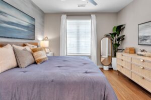 Modern bedroom with cozy bedding, large window, stylish dresser, and decorative plants, creating a serene, inviting space.