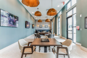 Modern lounge with elegant seating, hanging lamps, wall-mounted TVs, and a chessboard on the table. Bright and inviting space.