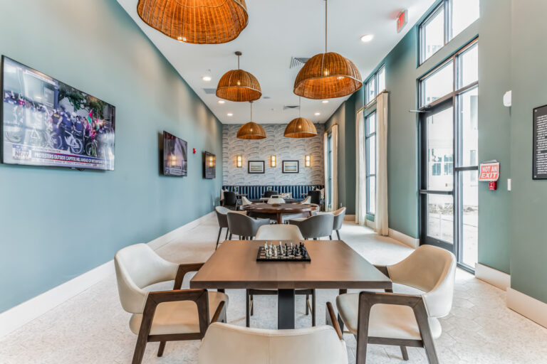 Modern lounge with elegant seating, hanging lamps, wall-mounted TVs, and a chessboard on the table. Bright and inviting space.