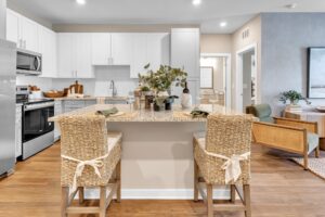 Modern kitchen interior with a central island, wicker chairs, and white cabinets. Cozy and inviting design.