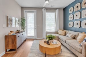 Modern living room with beige sofa, round wood table, and geometric wall art, featuring natural light and plants.