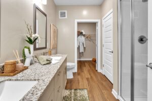 Modern bathroom with granite countertop, wooden floor, and stylish decor, featuring a walk-in closet and glass shower.