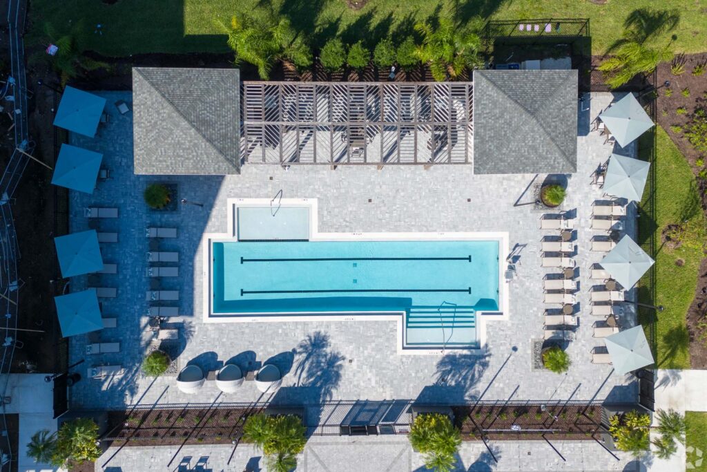 Aerial view of a modern swimming pool with lounge chairs and umbrellas surrounded by greenery.