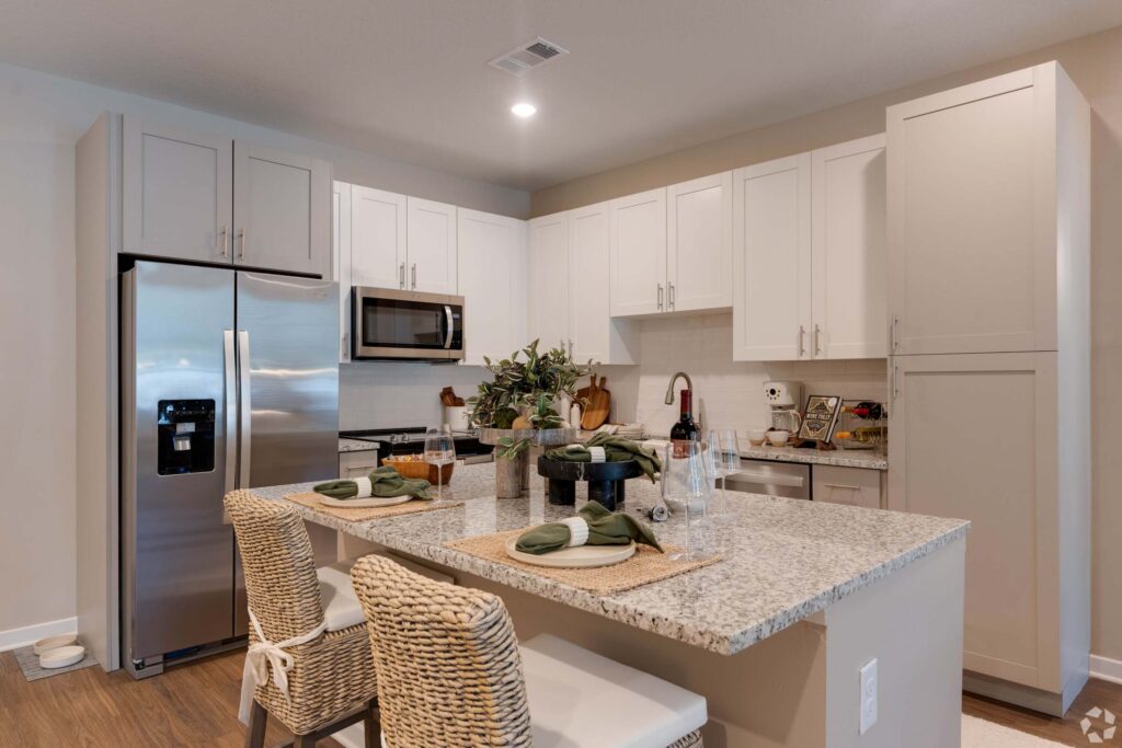 Modern kitchen with granite island, wicker chairs, stainless appliances, and elegant table setting.