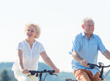Senior couple enjoying a leisurely bike ride outdoors under a clear sky.